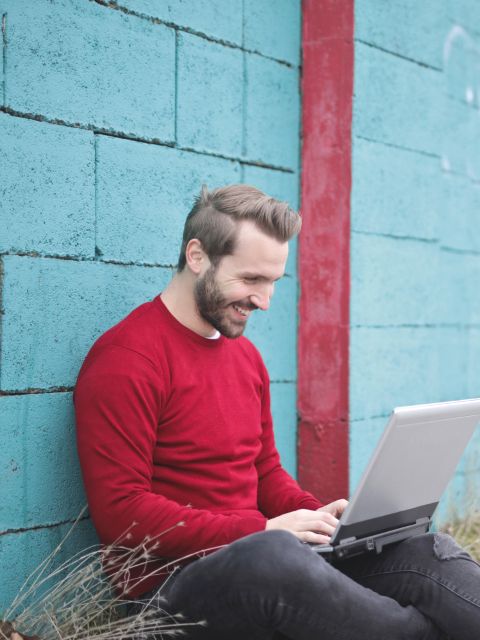 Freelancer in a red sweater working on a laptop against a teal wall